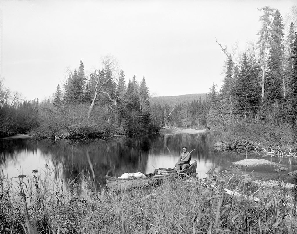 Un des guides autochtones de George T. Taylor assis dans un canoë rempli de provisions et d’équipement photographique, 1862.