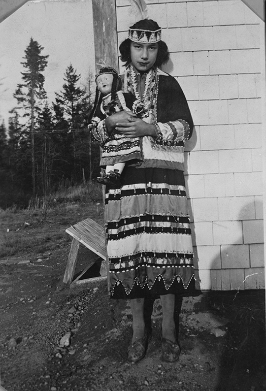 Mi’kmaw Girl in traditional dress holding doll wearing similar dress